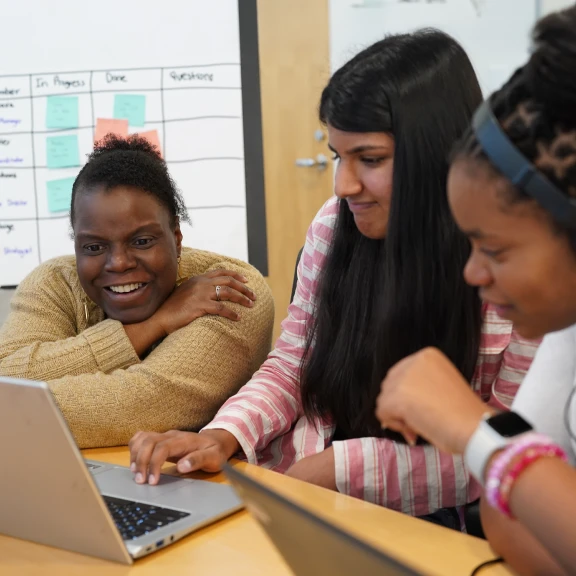 An adult mentor and two students work together around a laptop.